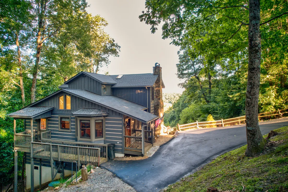 This exterior angle displays the retreat's wooden deck, large windows, and a striking stone chimney, all cocooned by nature. The inviting outdoor space suggests areas for gathering, watching sunsets, or relaxing together under the stars.