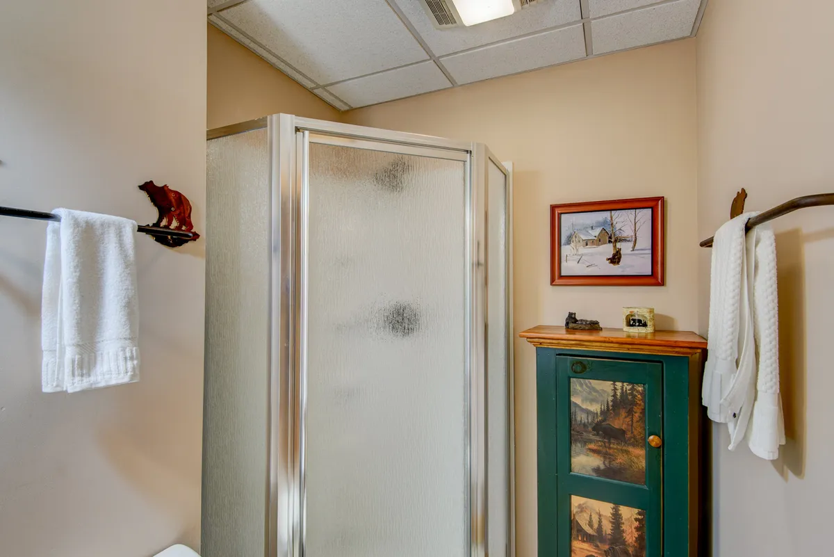 This image presents a stylish bathroom interior with a glass shower enclosure, green vanity, and wall art. The mood is comfortable and homey, suggesting easy access for guests seeking convenience during gatherings.