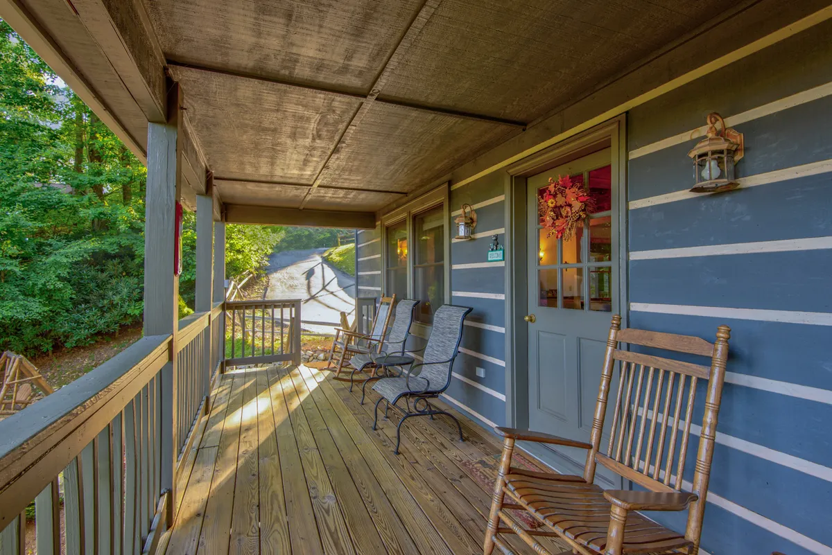 The image features two classic rocking chairs set on a welcoming front porch, decorated with a charming wreath and lanterns, inviting guests to sit and take in the peaceful surroundings. The vantage point suggests a quiet, intimate space perfect for relaxation and enjoying the outdoors together.