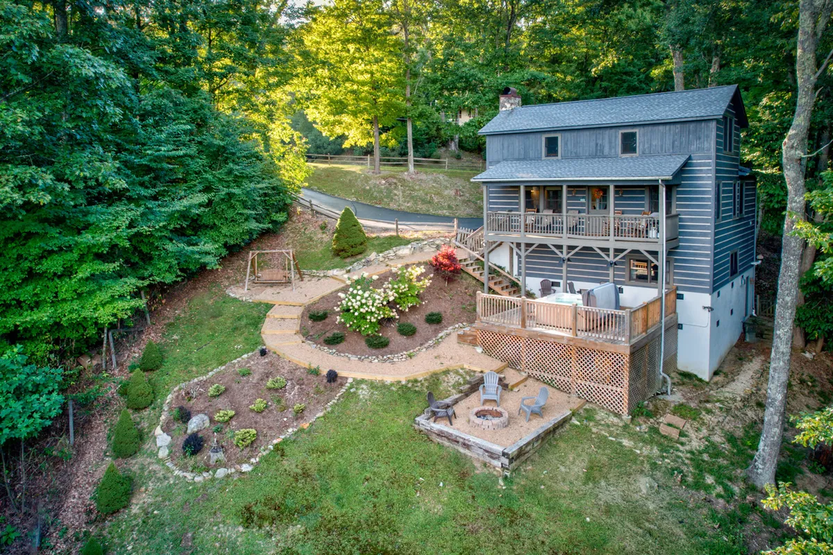 The hero image shows a welcoming mountain cabin nestled amid lush landscaping, with a spacious deck perfect for sunsets, a cozy fire pit area ideal for evening gatherings, and a playful swing set inviting families to relax and make memories together. The peaceful outdoor scene radiates both charm and comfort, surrounded by natural beauty and tailored for quality time outdoors.