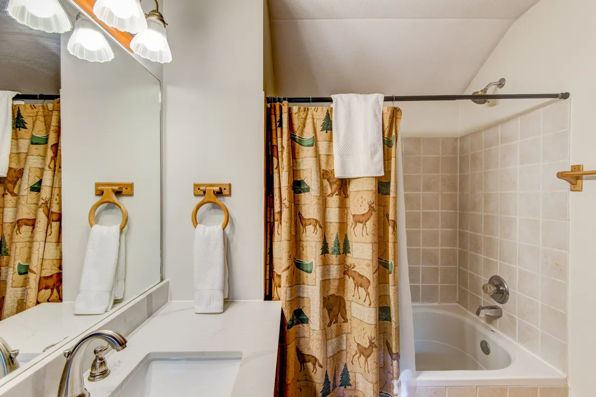 A bright and warm bathroom with a bathtub, shower curtain, sink, and large mirrors. The space feels inviting and ideal for relaxing in a soothing bath or preparing for the day ahead.