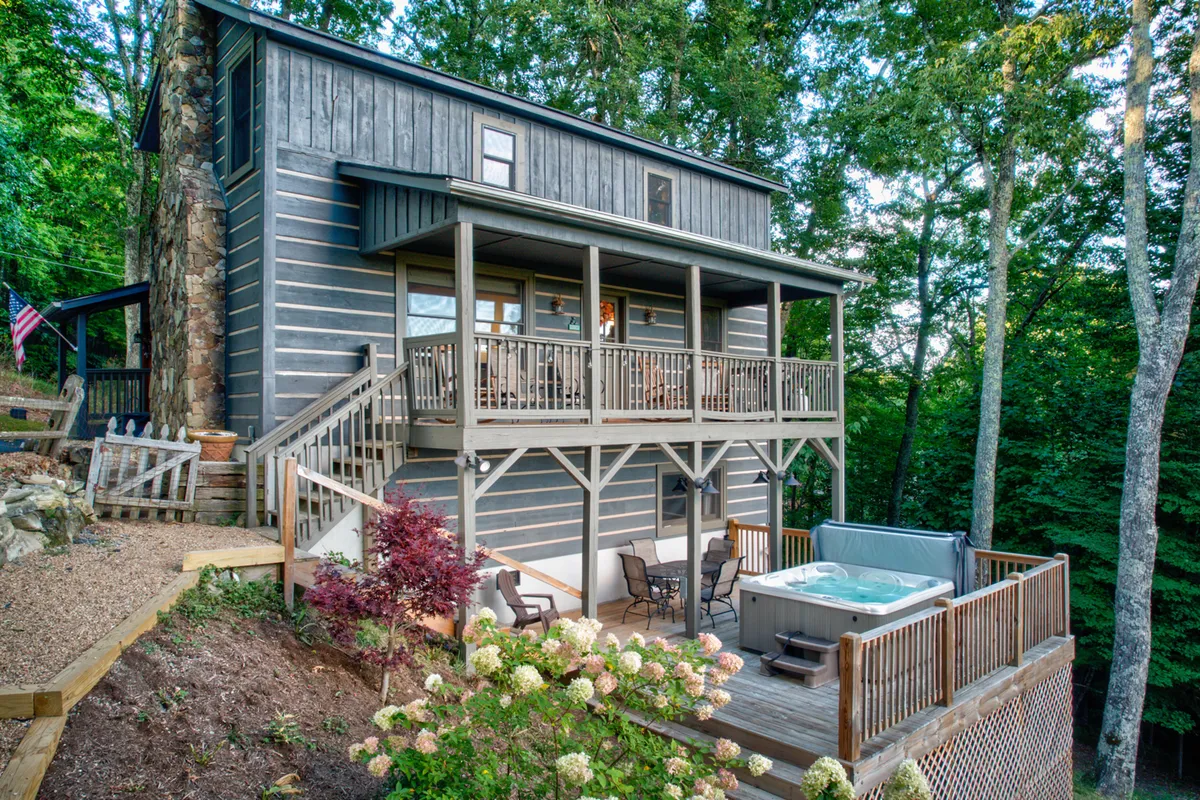 An inviting wooden deck set amidst lush greenery, featuring a hot tub, stone wall, and comfortable outdoor seating. The space is designed for relaxation after outdoor activities, with the hot tub offering a luxurious way to unwind while staying immersed in nature.