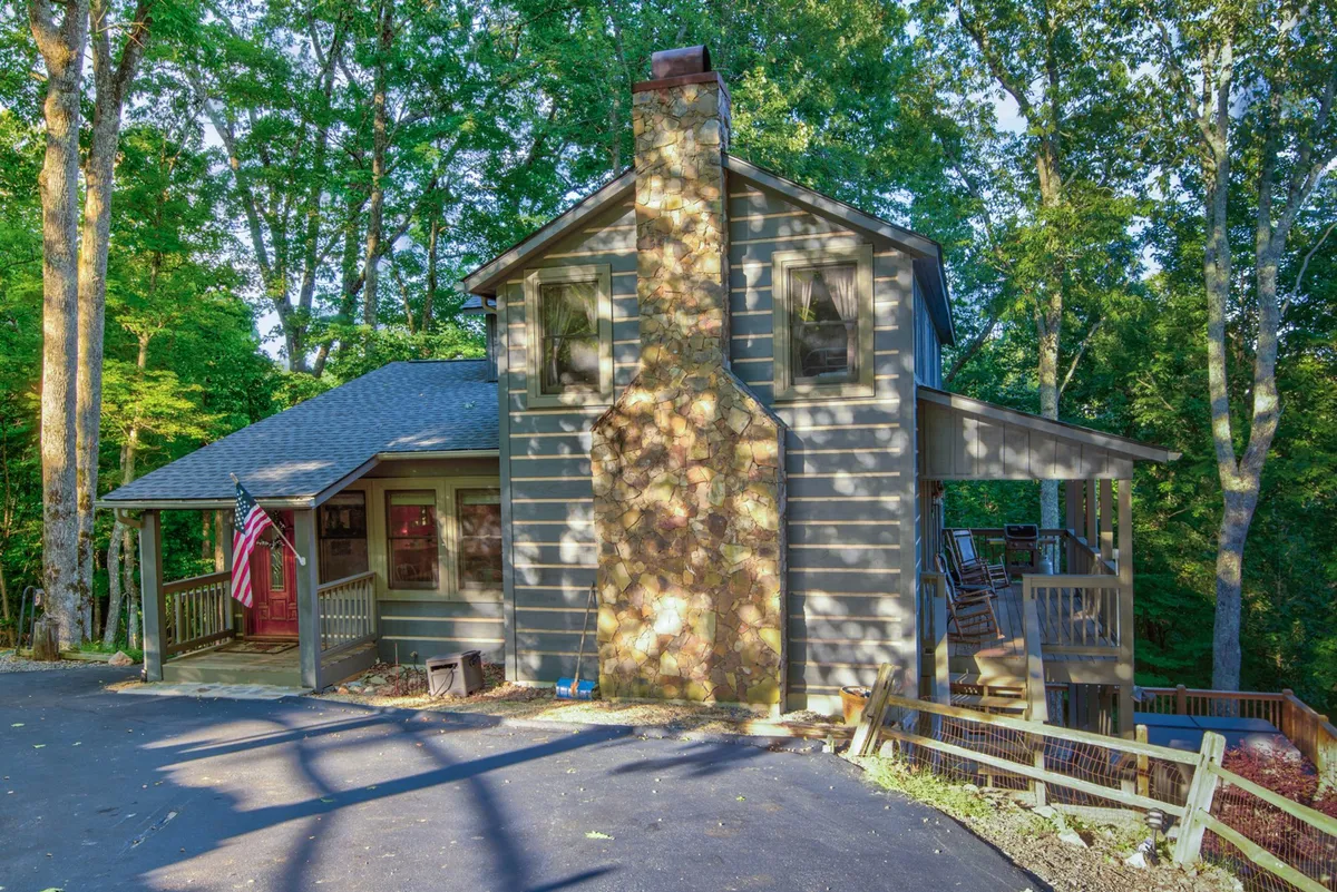 A welcoming exterior view featuring a wooden deck, stone chimney, and an American flag. The scene radiates a cozy, inviting atmosphere and suggests the deck as a prime spot for family gatherings, outdoor meals, or evenings after a day of exploring local attractions.