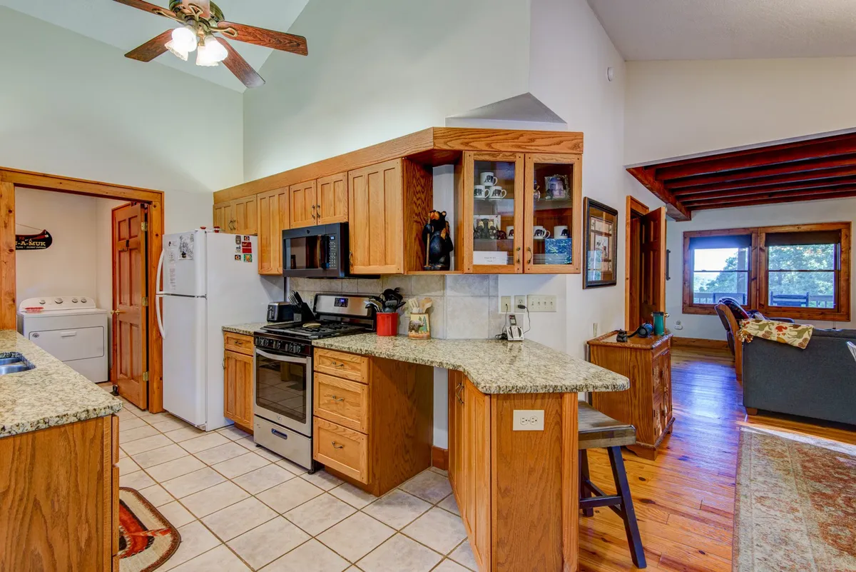 A spacious kitchen with a large granite countertop, warm wooden cabinetry, stainless steel appliances, and an open layout that flows into the adjoining dining and living areas. The space feels bright and comfortable, offering plenty of room for multiple people to cook, gather, and converse.