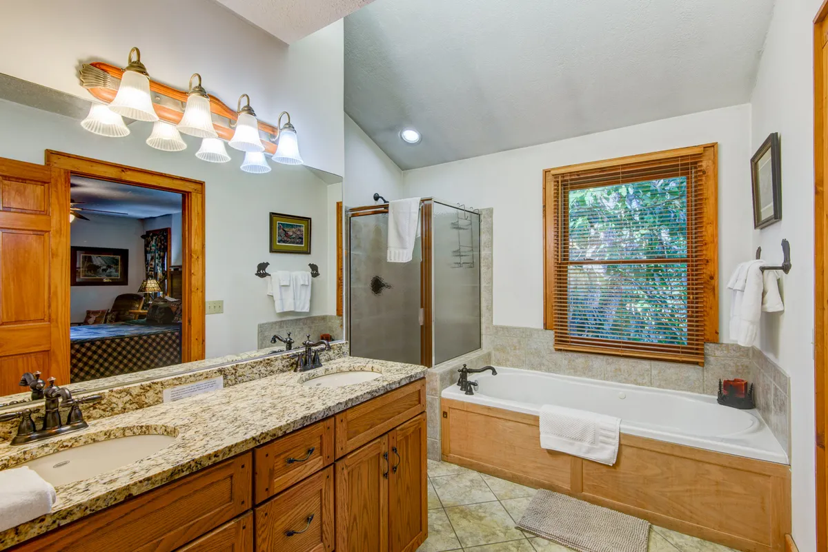 A luxurious bathroom featuring a double vanity with granite countertop, a spacious shower enclosure, a bathtub, and a large window that lets in abundant natural light. The design exudes a calming and serene mood, perfect for relaxation.