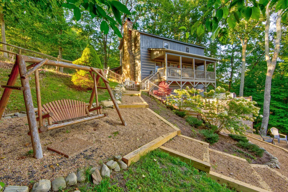 A view of the fenced, sloped yard with a swing set, the main deck above, and garden beds. The image presents a safe, family- and pet-friendly outdoor area, ideal for children and dogs to play while adults relax nearby. The yard's boundary is clearly visible, reinforcing the sense of security and fun.